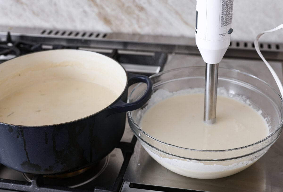 Side shot of half the soup mixture blended in a glass bowl with an immersion blender. 