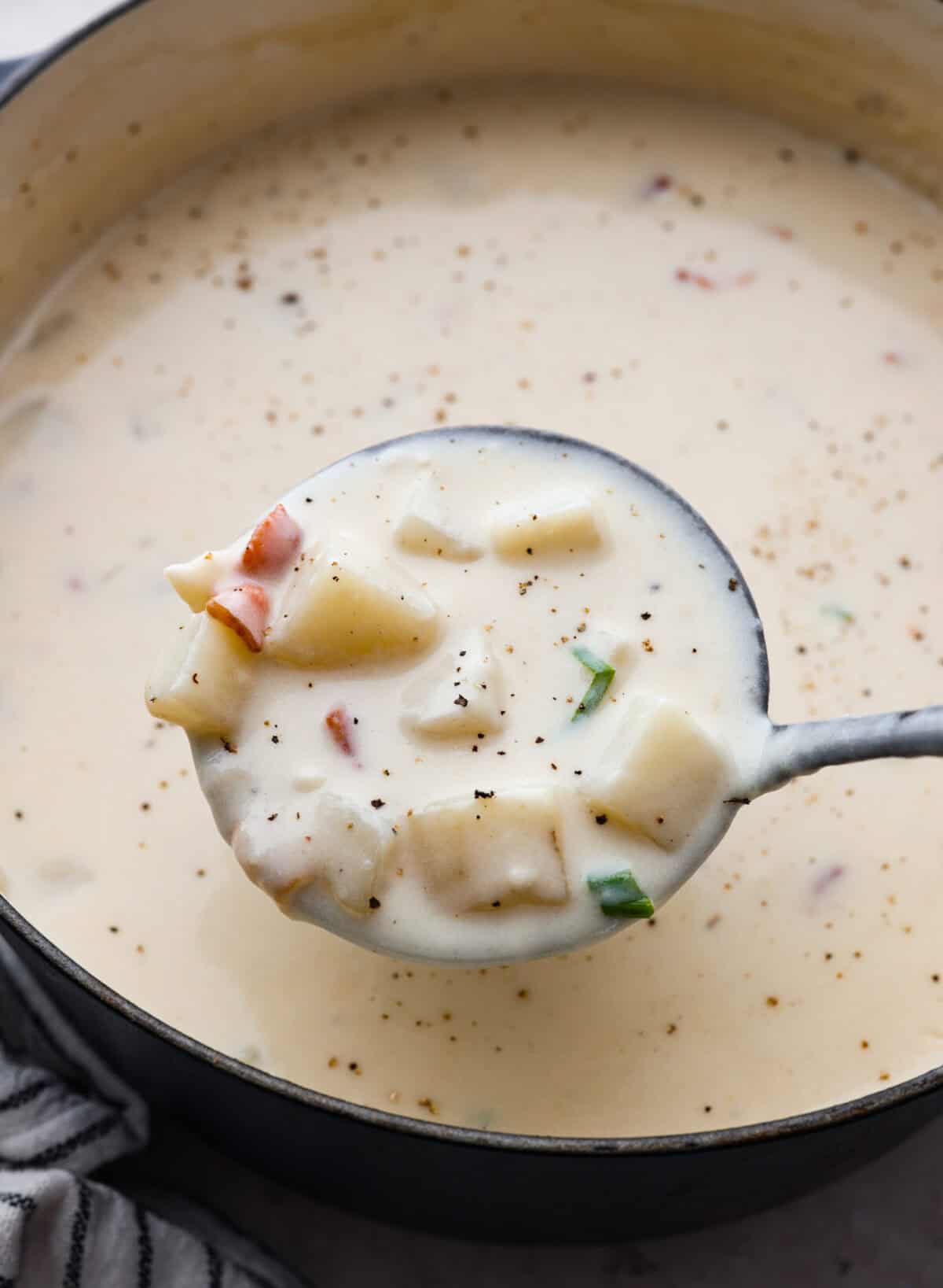 Close up shot of a ladle full of creamy potato soup over the pot full of soup. 