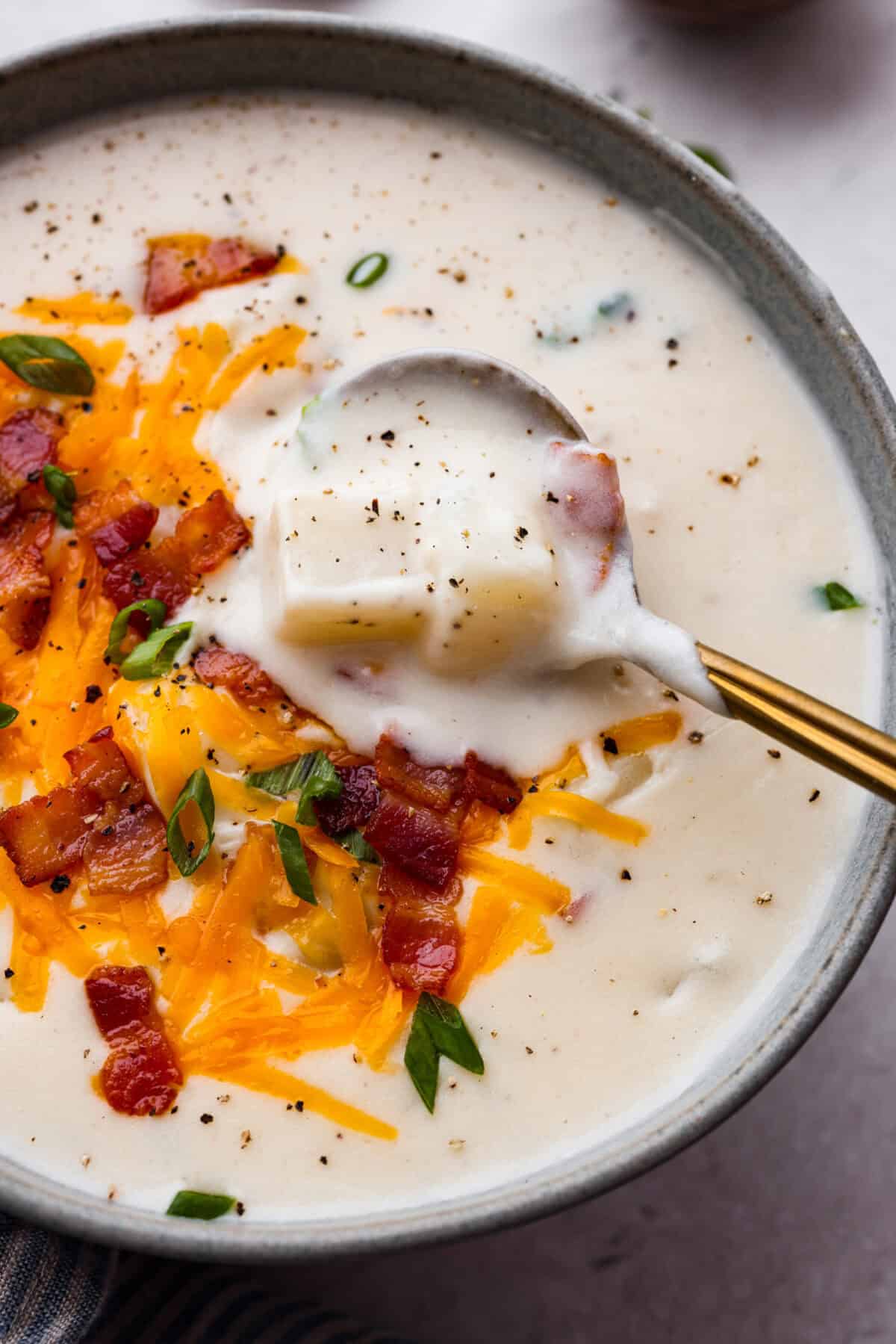 Overhead shot of a bowl of creamy potato soup with a spoon sopping a bit out of it. 