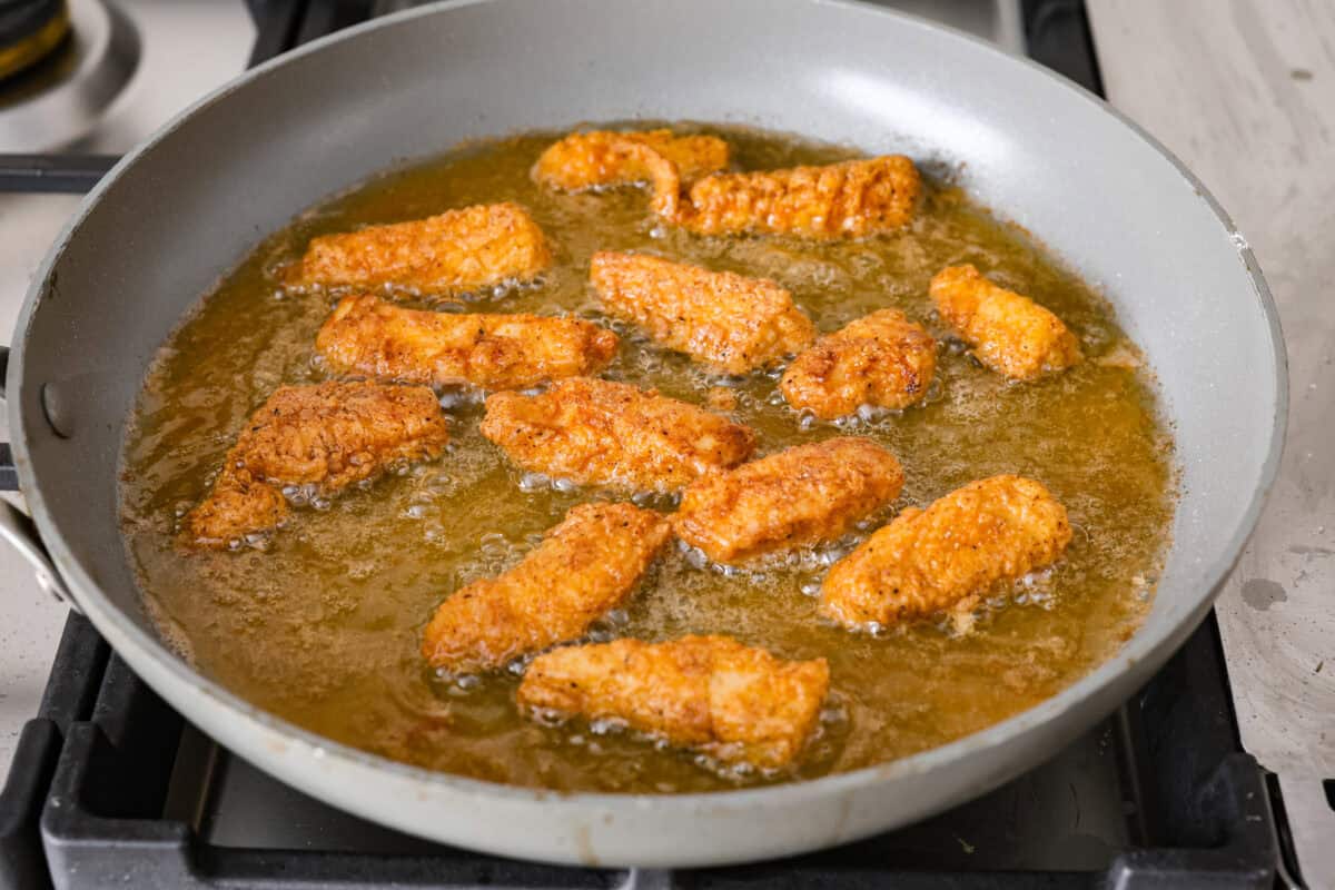 Angle shot of breaded chicken being fried in a skillet. 