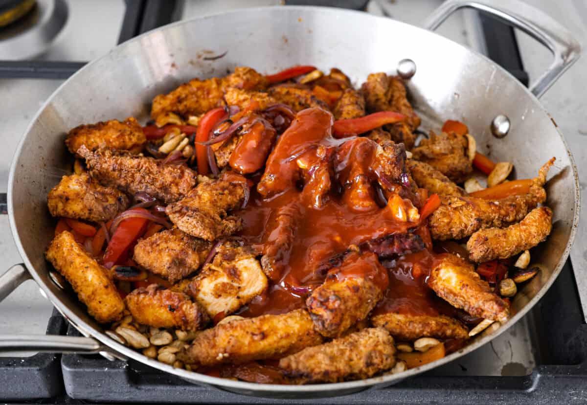 Close up shot of fried chicken, stir fried veggies covered in sauce in a wok. 