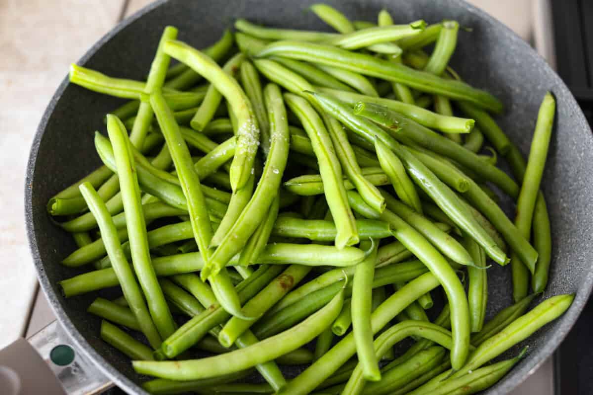 Overhead shot of green beans, salt and water in a skillet. 