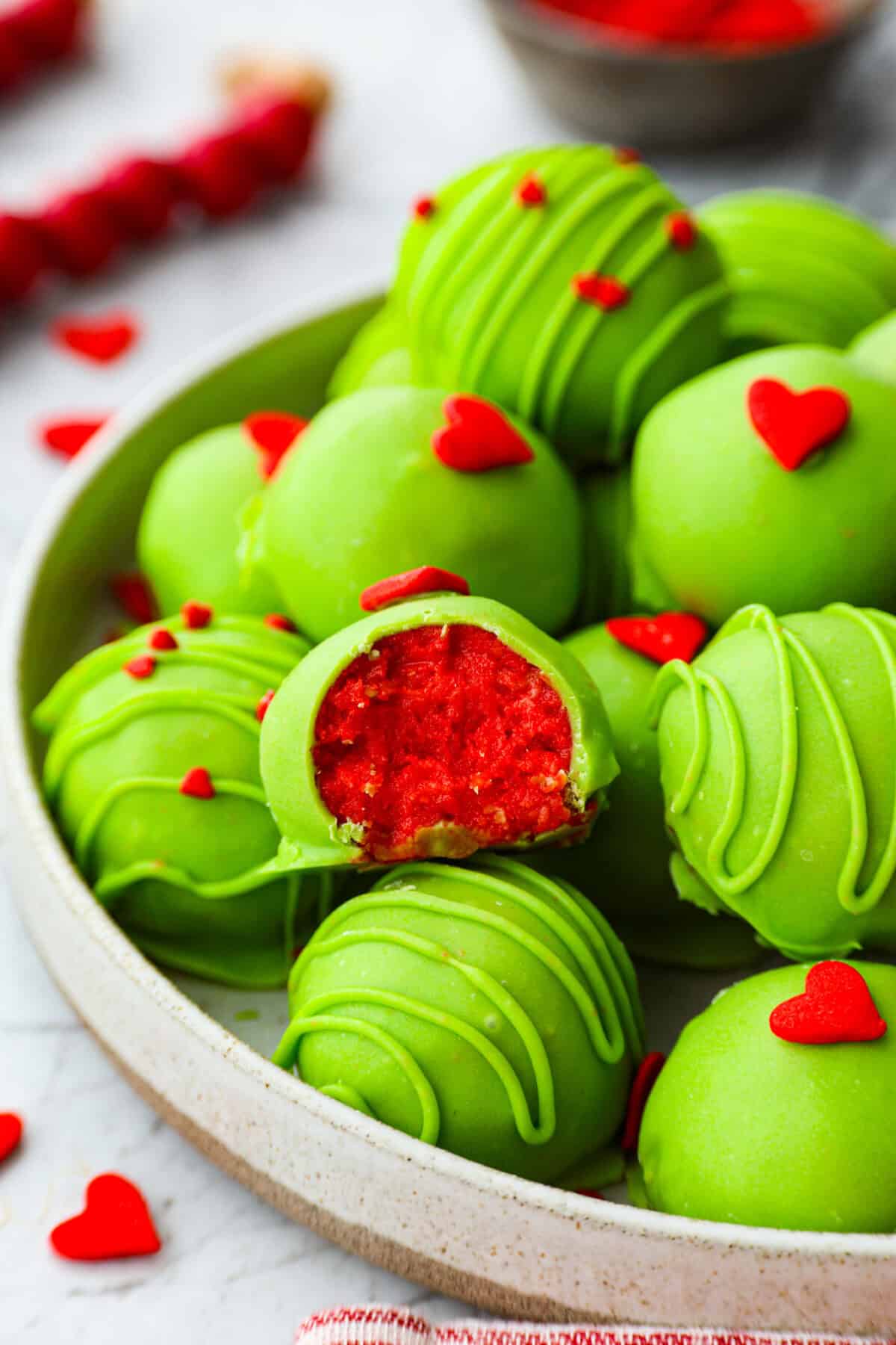 Angle shot of Grinch Oreo balls on a serving platter with one that has a bte taken out of it. 