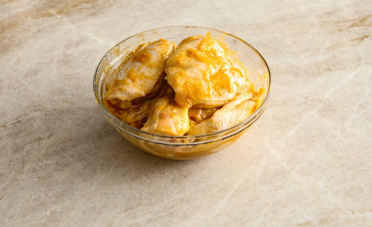 Angle shot of chicken thighs doused in sauce in a bowl.