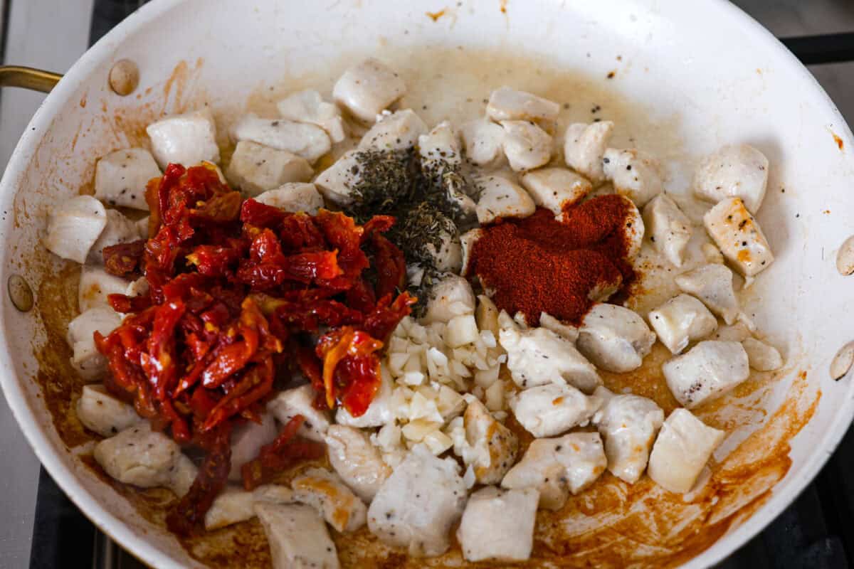 Overhead shot of sun-dried tomatoes, garlic and seasonings being added to the chicken cooking in a skillet. 