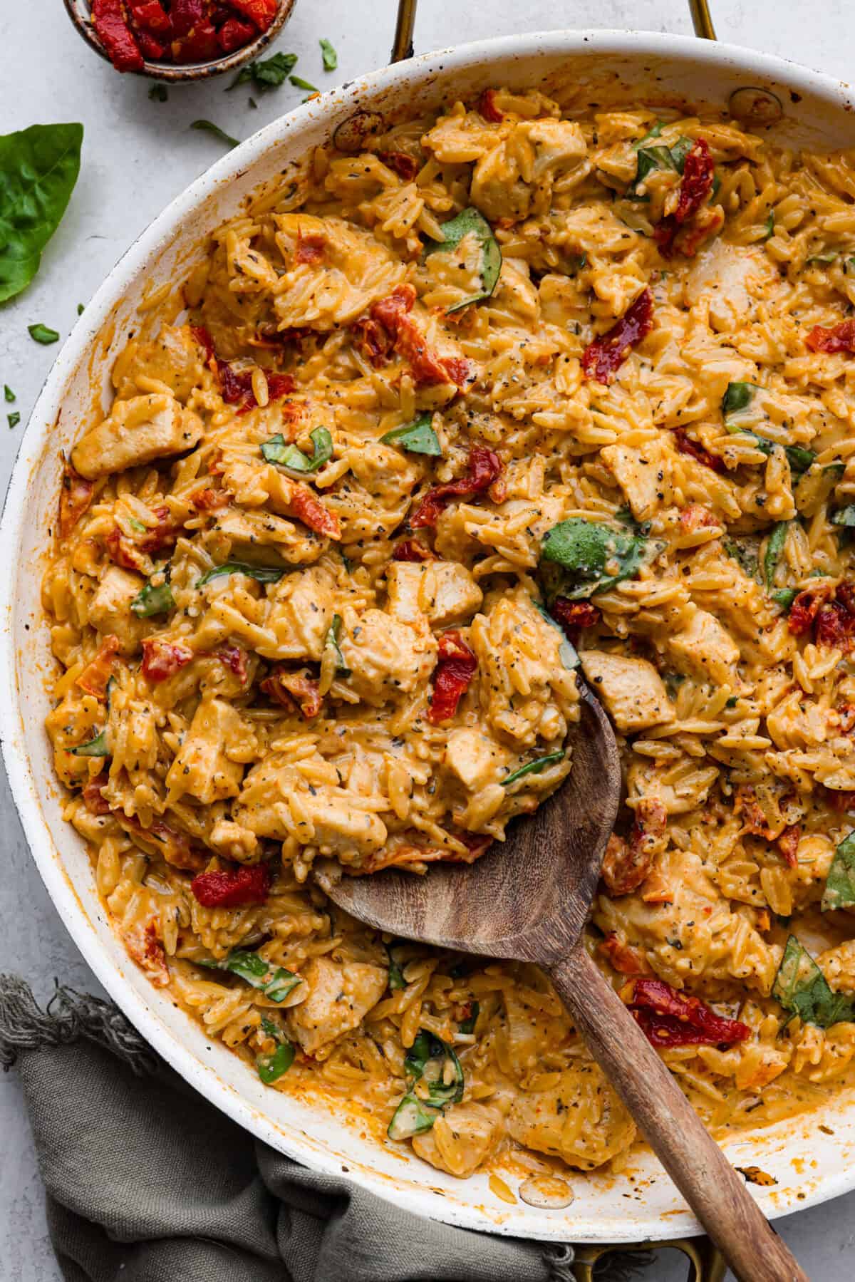 Overhead shot of marry me chicken orzo in a skillet with wooden serving spoon. 