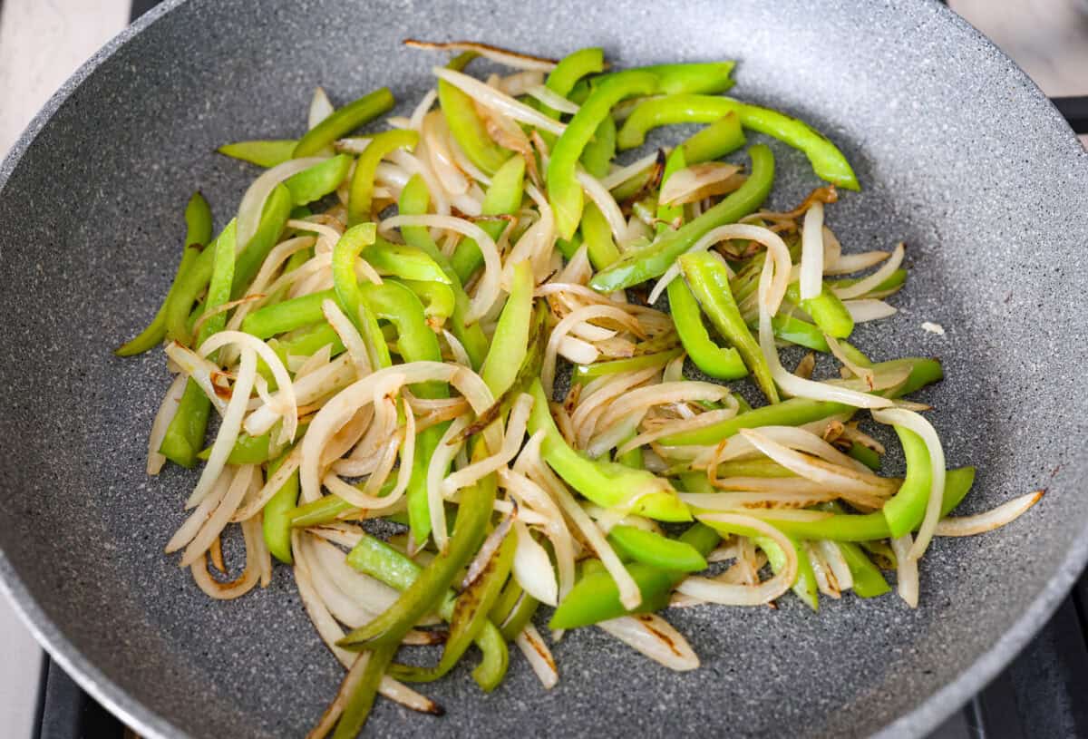 Overhead shot of onions and green peppers cooking in a skillet.