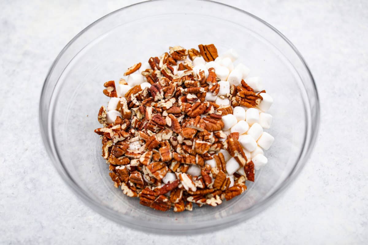 Overhead shot of pecans with mini marshmallows in a glass bowl. 