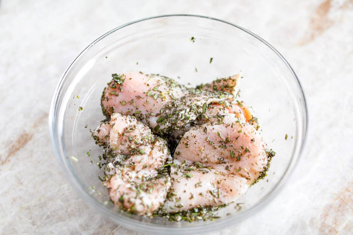 Overhead shot of chicken breasts with olive oil, lemon juice rosemary salt and pepper in a bowl. 