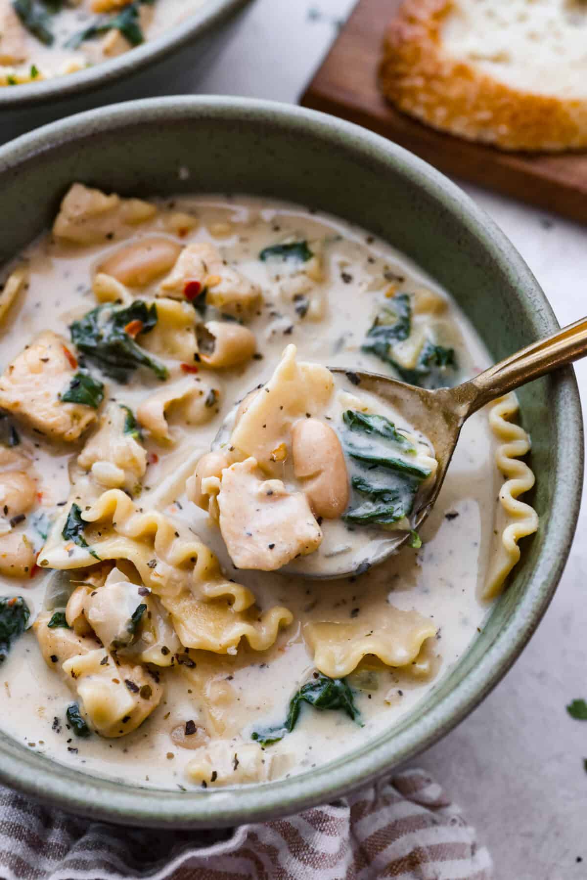 Close up shot of a bowl of white lasagna soup with a spoon lifting a bite out.