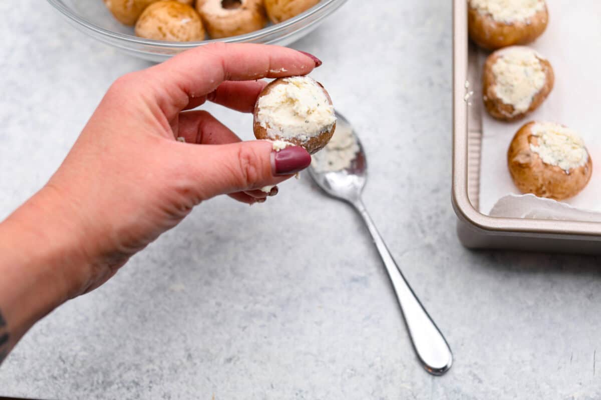 Overhead shot of someone holding a mushroom with Boursin cheese stuffed into the opening. 