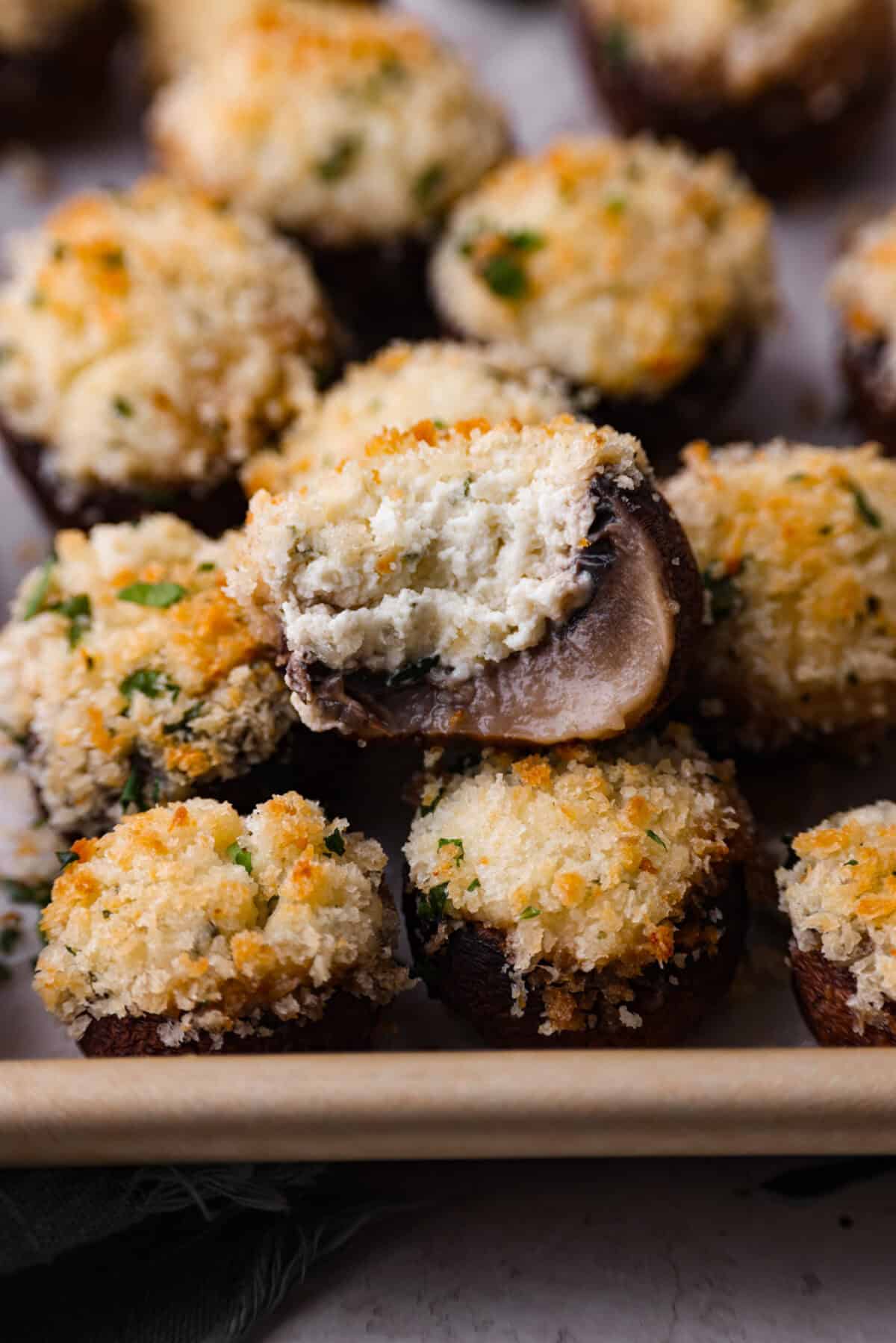 Close up shot of Boursin stuffed mushrooms, one has a bite out of it. 