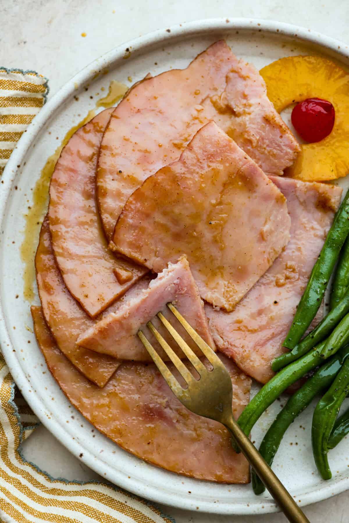 Close up shot of plated brown sugar pineapple glazed ham next to green beans, a pineapple ring and a cherry. 