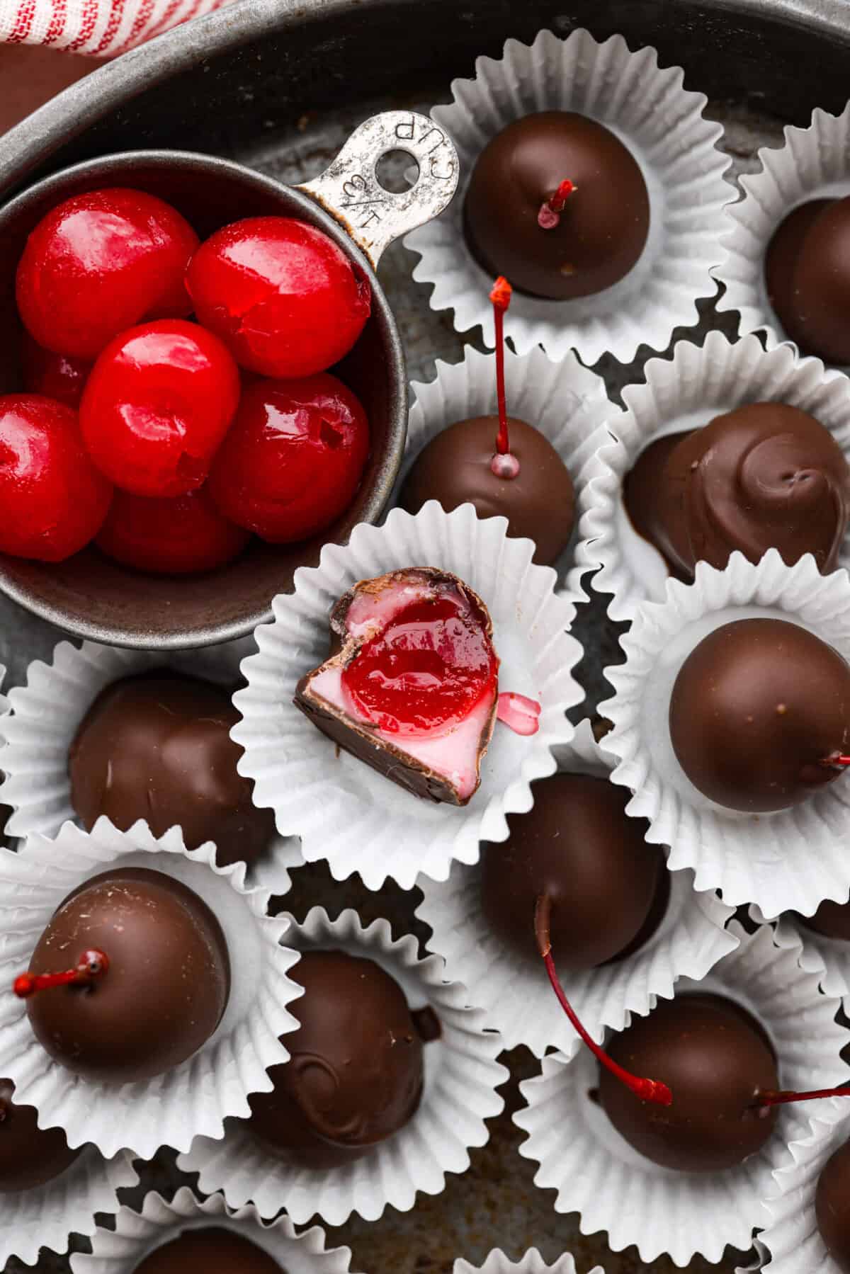 Overhead shot of cherry cordials in paper wrappers with one that has a bite taken out. 