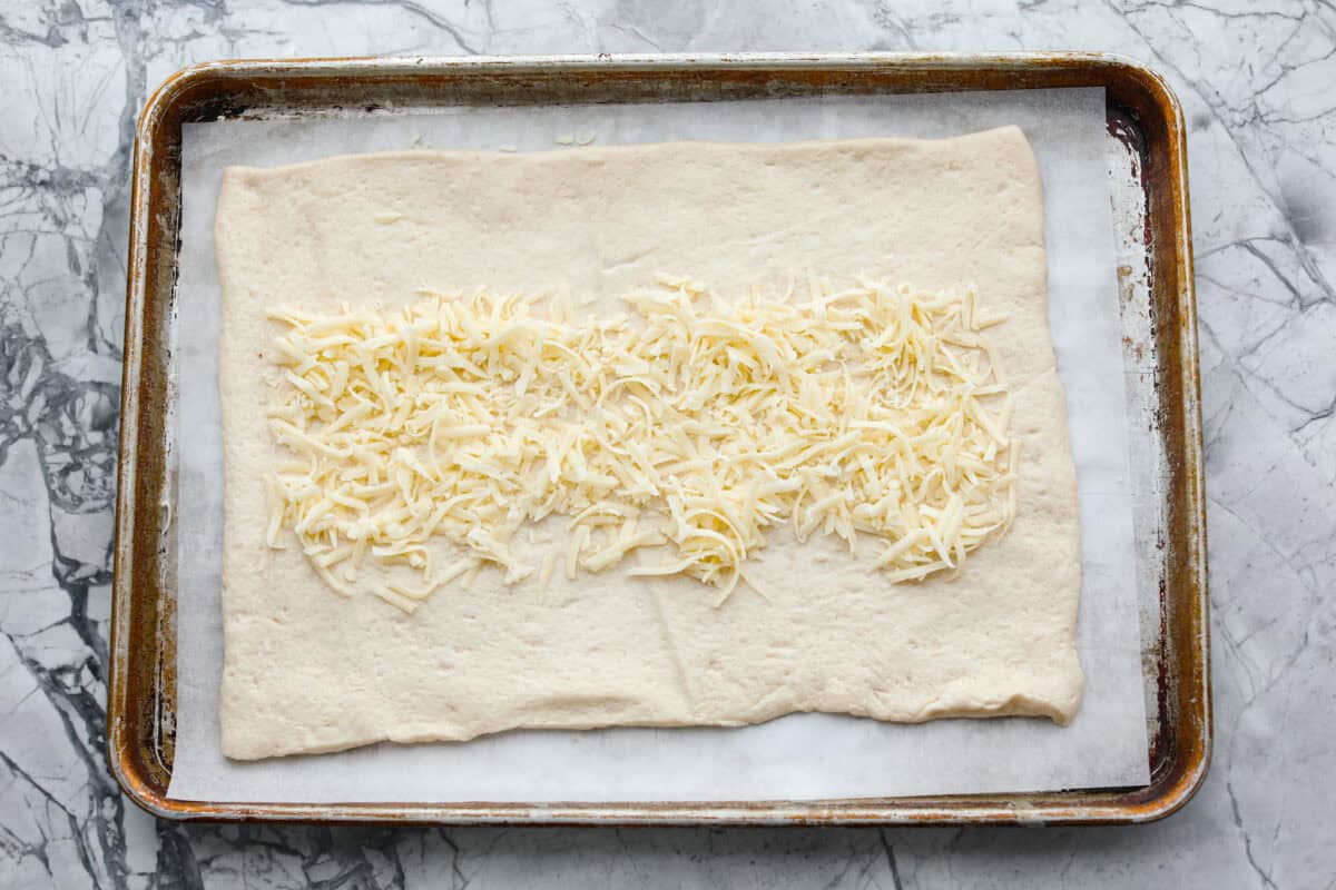 Overhead shot of the canned pizza dough rolled out with mozzarella cheese down the middle all on parchment-lined cookie sheet.