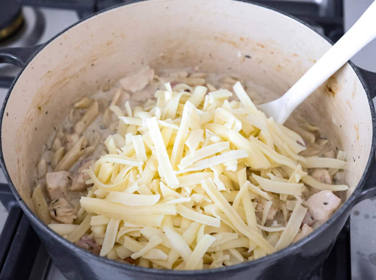 Angle shot of cheese added to the chicken cordon bleu pasta in the pot. 