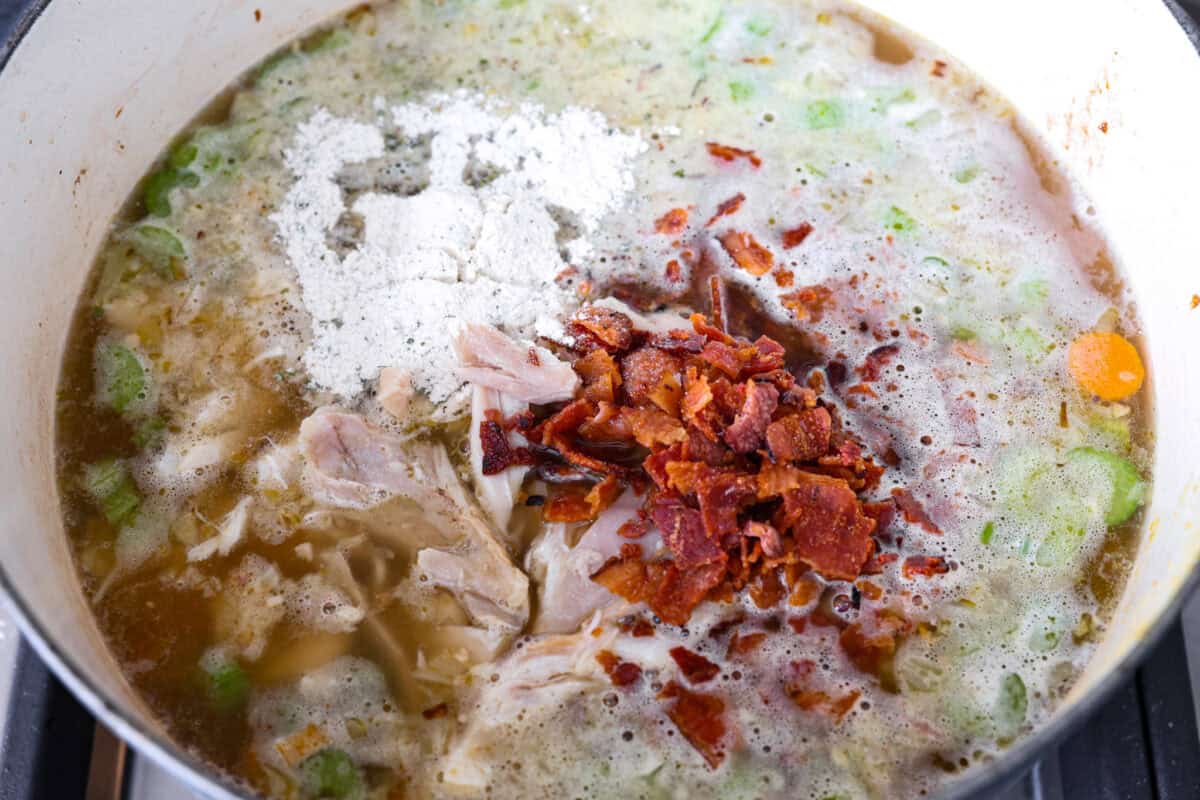 Overhead shot of broth, ranch packet, shredded chicken and bacon in the same pot with the veggies. 