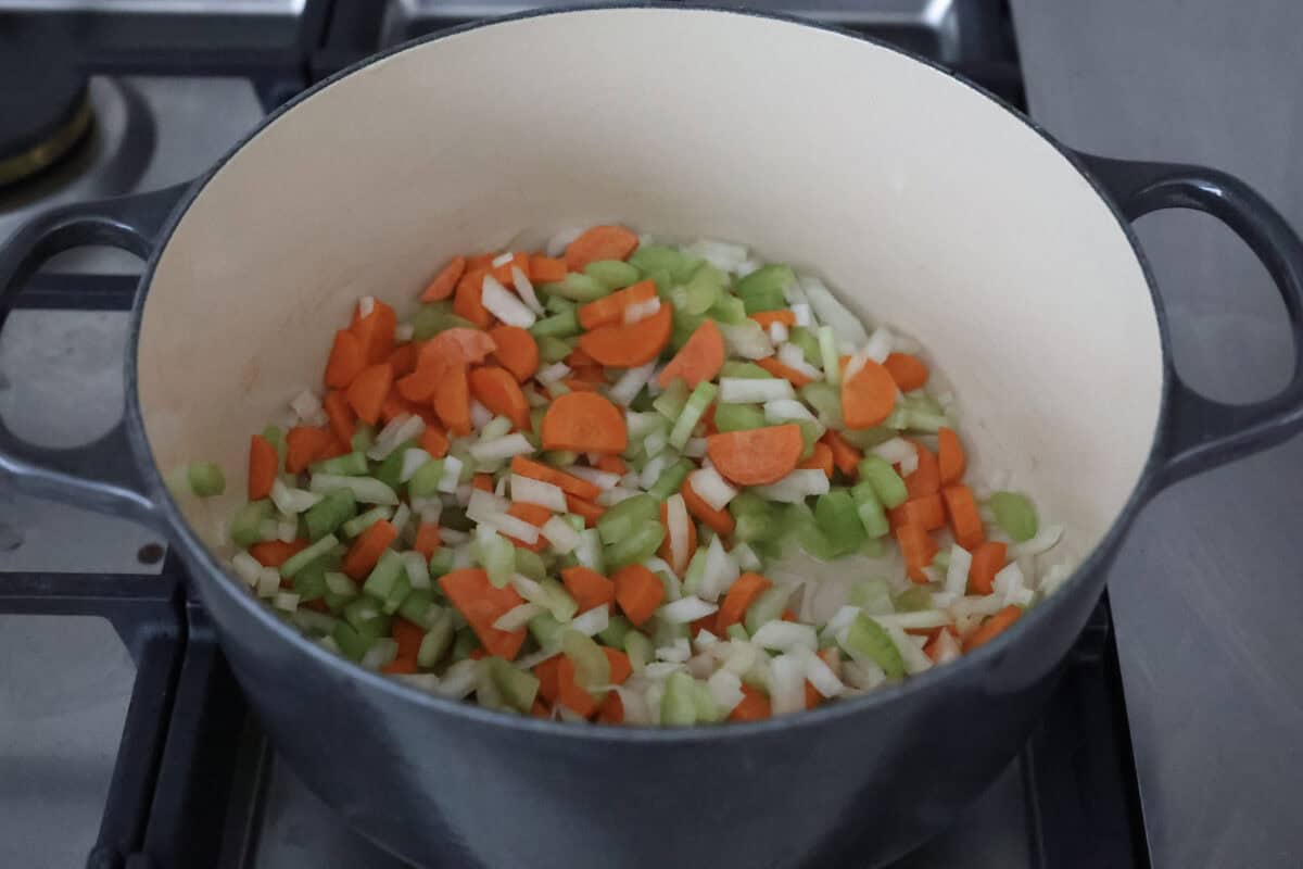 Angle shot of carrots, celery and onions cooking in a pot on the stove. 