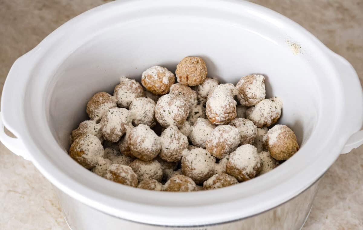 Angle shot of frozen meatballs with seasoning packets sprinkled over the top in a crockpot. 