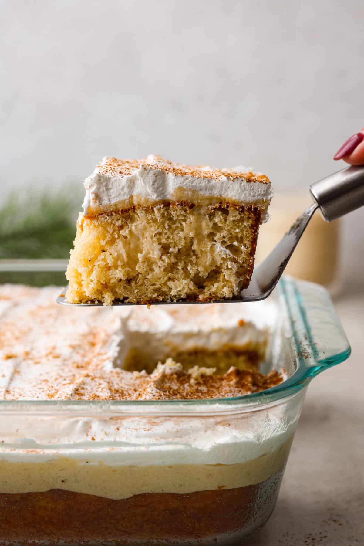 Side shot of a piece of eggnog poke cake being lifted out of the baking dish. 