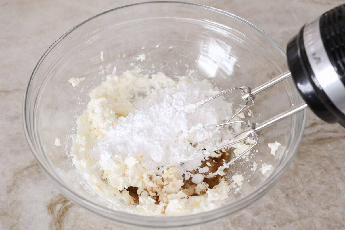 Overhead shot of someone using a hand mixer to mix the frosting ingredients together in a bowl. 