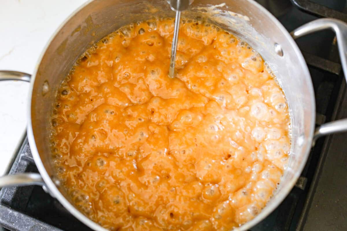 Overhead shot of pot with bubbling caramel and a candy thermometer sticking out of it. 