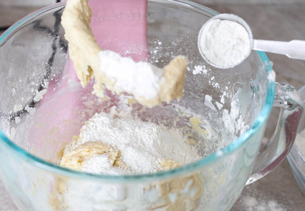 Angle shot of ingredients added to a mixing bowl, and someone added flour one tablespoon at a time. 