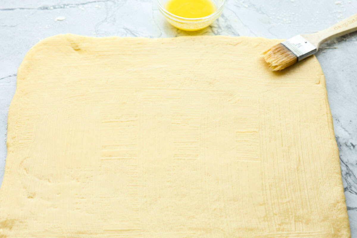 Overhead shot of rectangular slap of rolled out dough with butter smothered on top. 