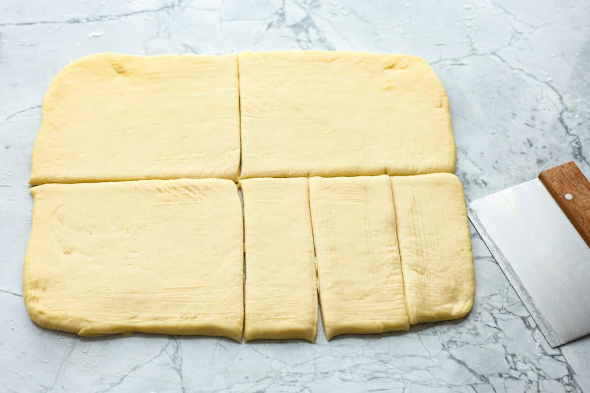 Overhead shot of rectangular dough cut into fourths and then one of the fourth cut into thirds. 