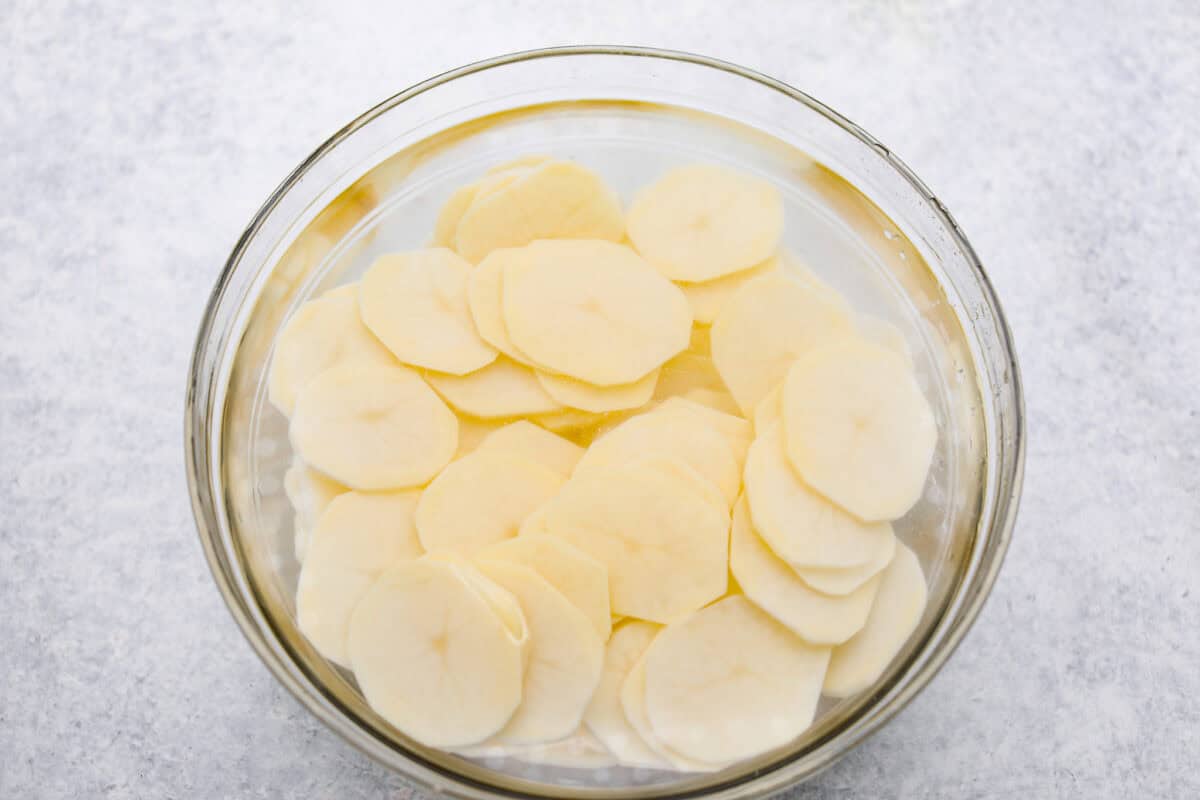 Overhead shot of potato slices in a bowl of cold water. 