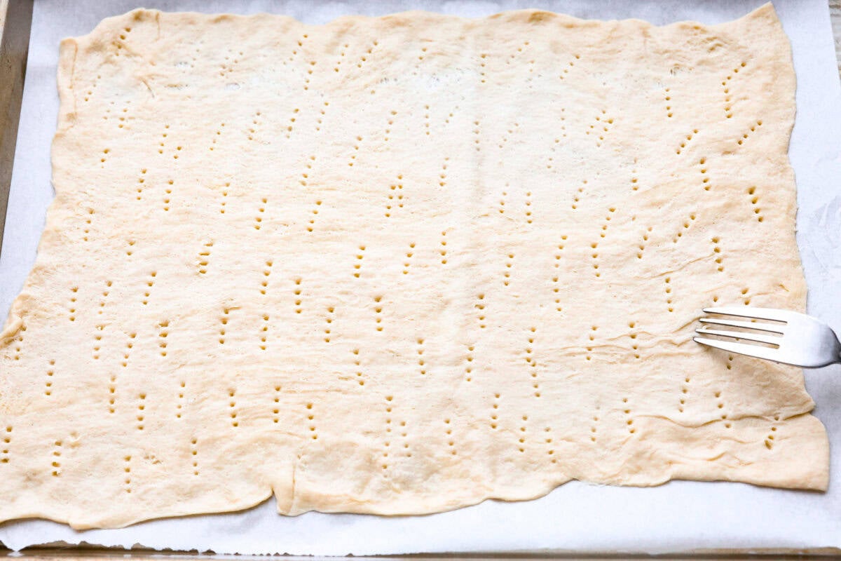 Overhead shot of crescent sheet dough being pricked a bunch with a fork. 