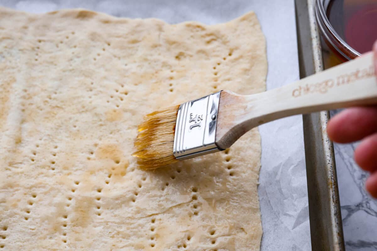 Angle shot of someone spreading maple syrup on the crescent dough sheet. 