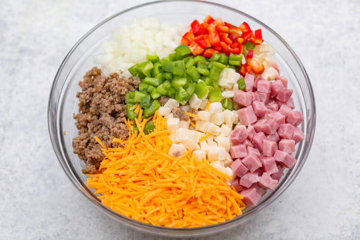 Overhead shot of dived veggies, ham, sausage and cheese in a bowl. 