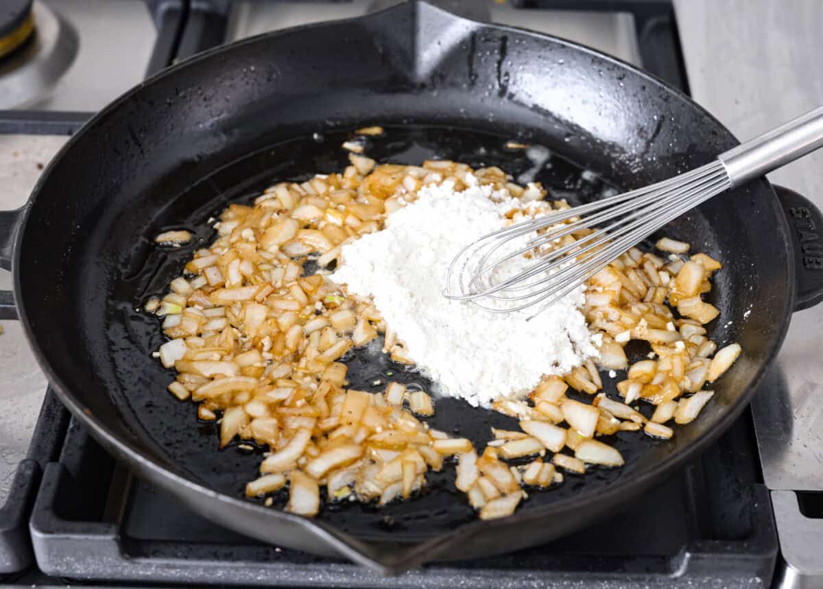 Angle shot of flour being stirred into the cooked onions. 