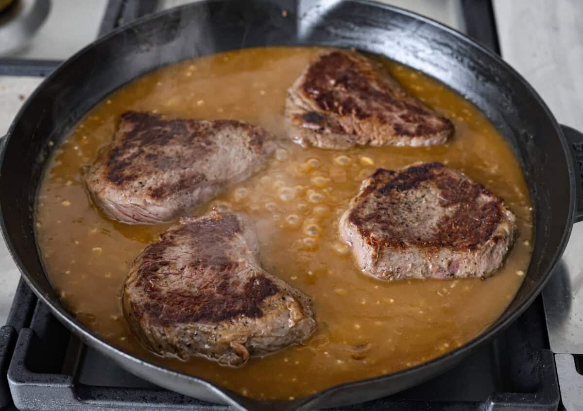 Angle shot of the steaks back in the gravy in the skillet. 