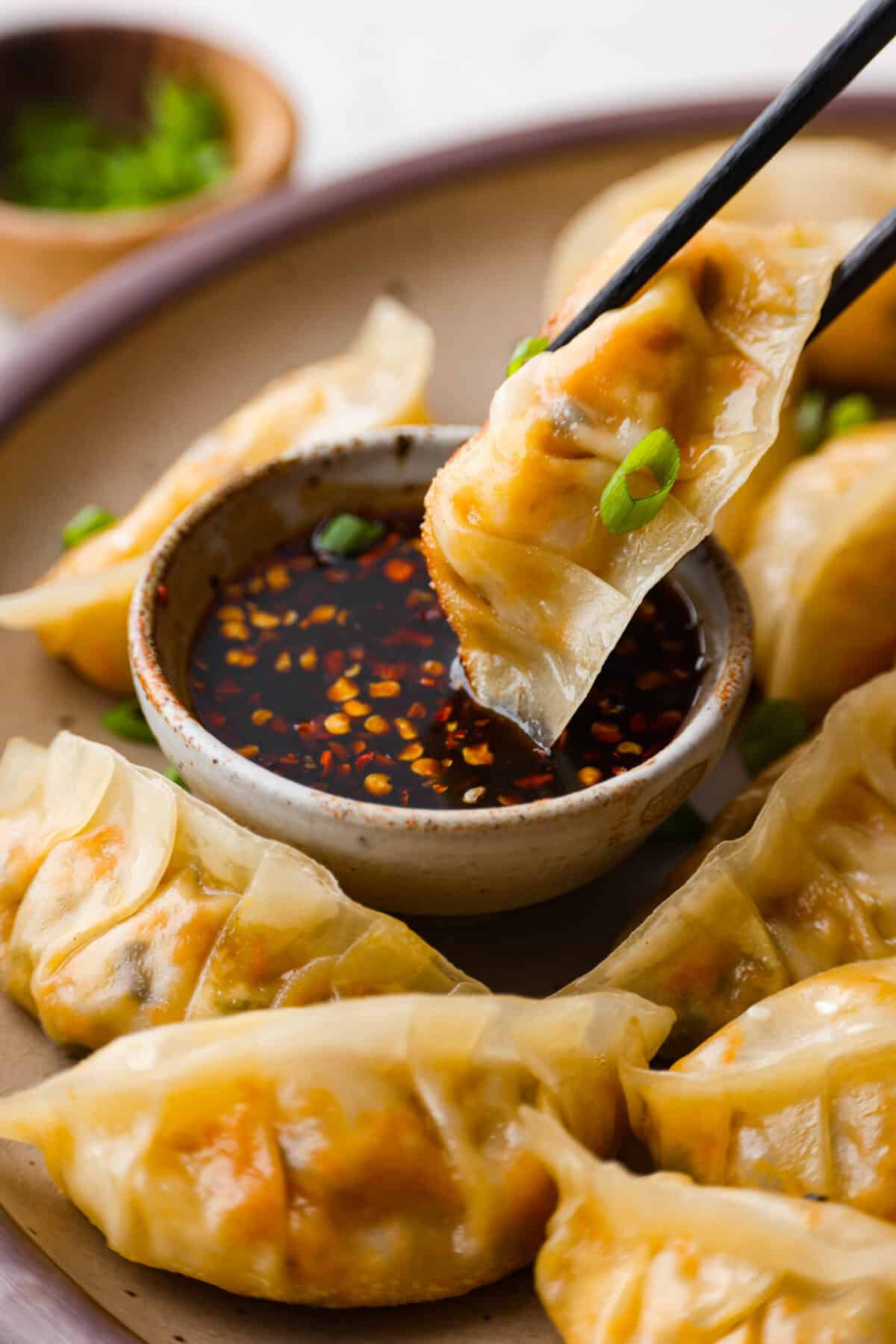 Close up whot of someone using chopsticks to dip a vegetable dumpling into some sauce. 