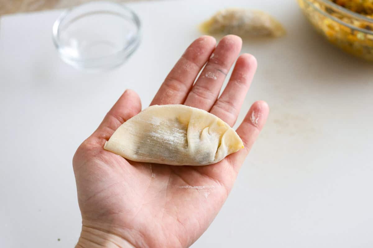 Overhead shot of someone holding the dumpling wrapper with filling and crimping the edges. 