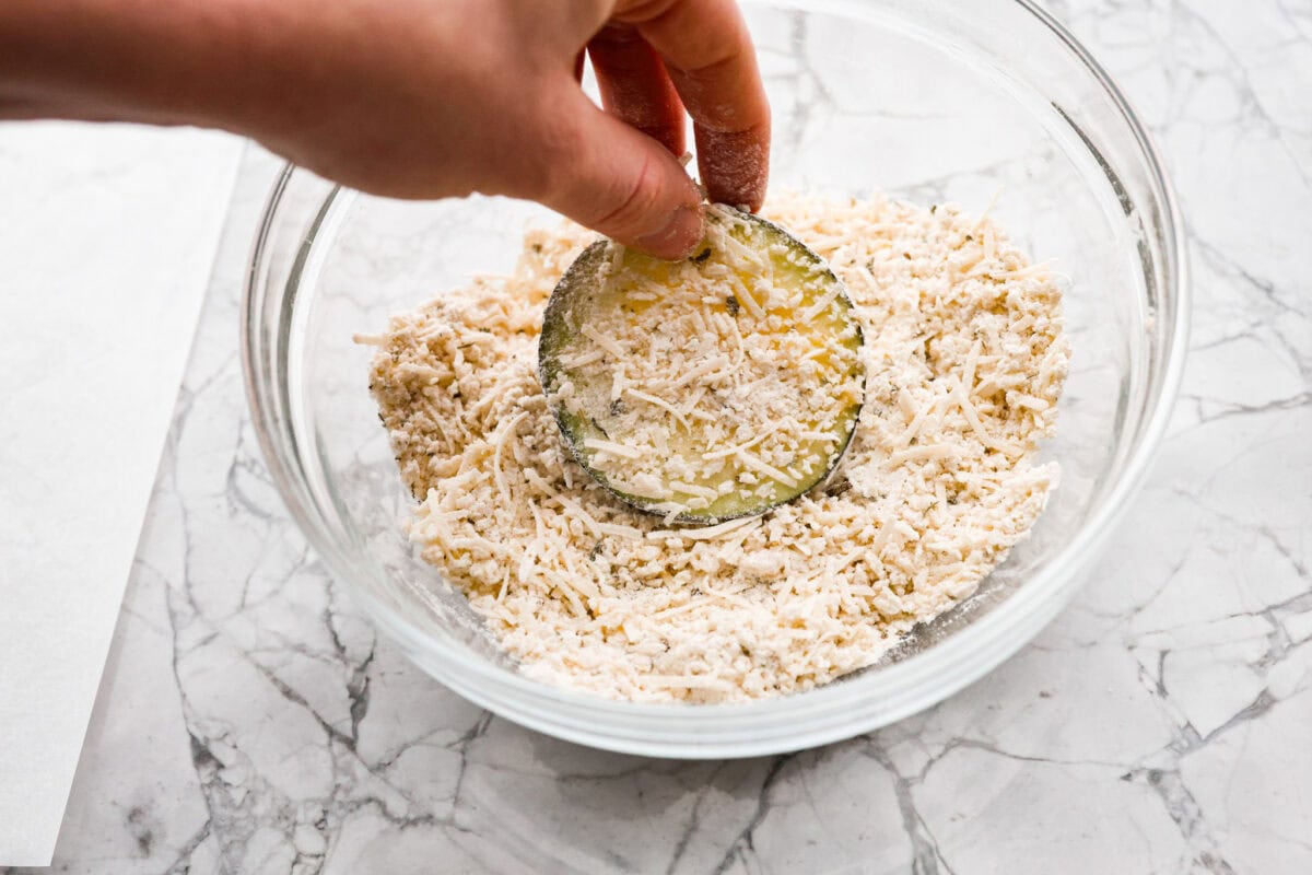 Overhead shot of someone dipping a slice of egg washed eggplant into breading mixture. 