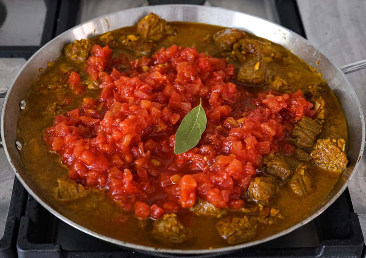 Angle shot of tomatoes and water added to the beef and onion mixture in the skillet. 