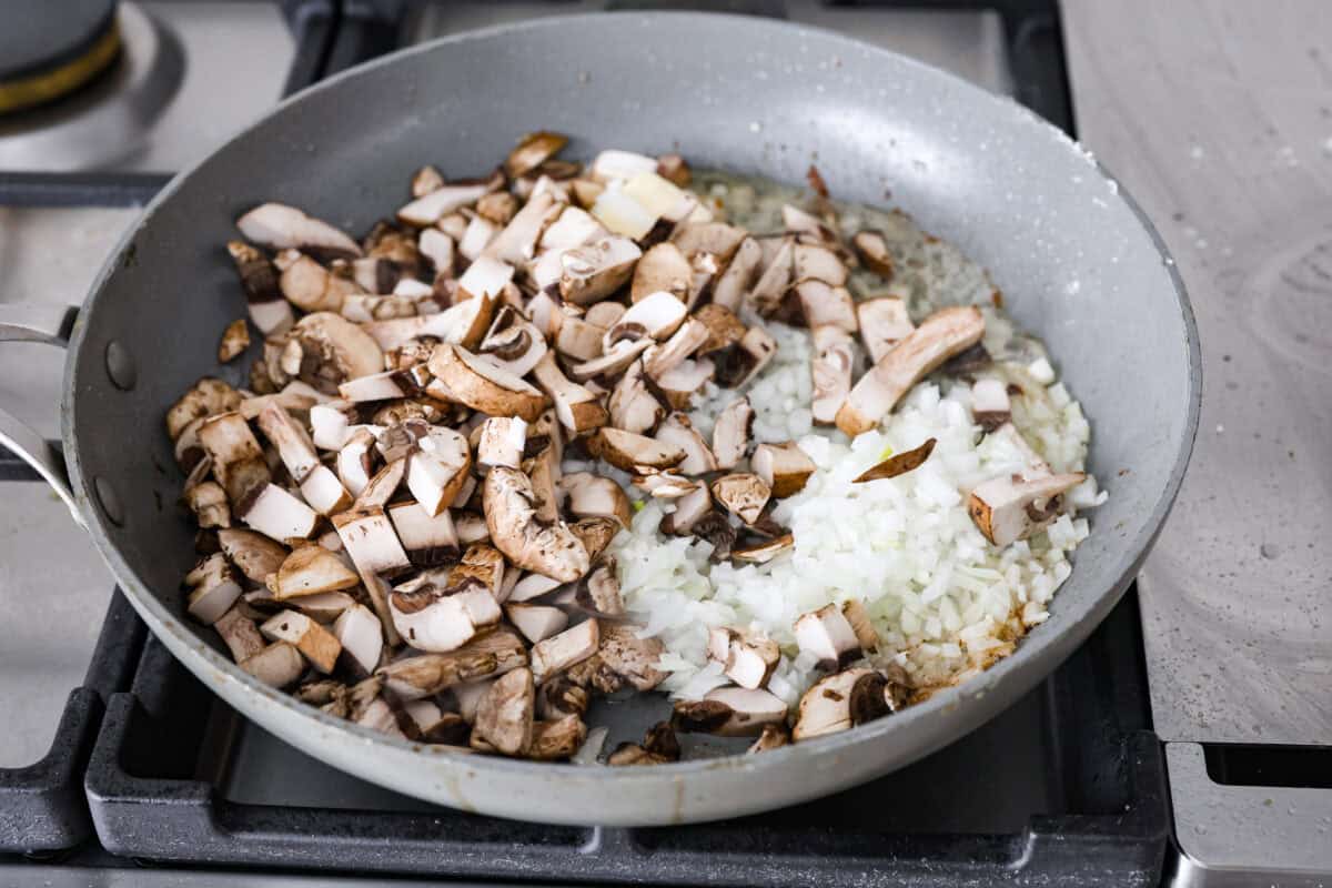 Angle shot of onions garlic and mushrooms cooking in butter in a skillet. 