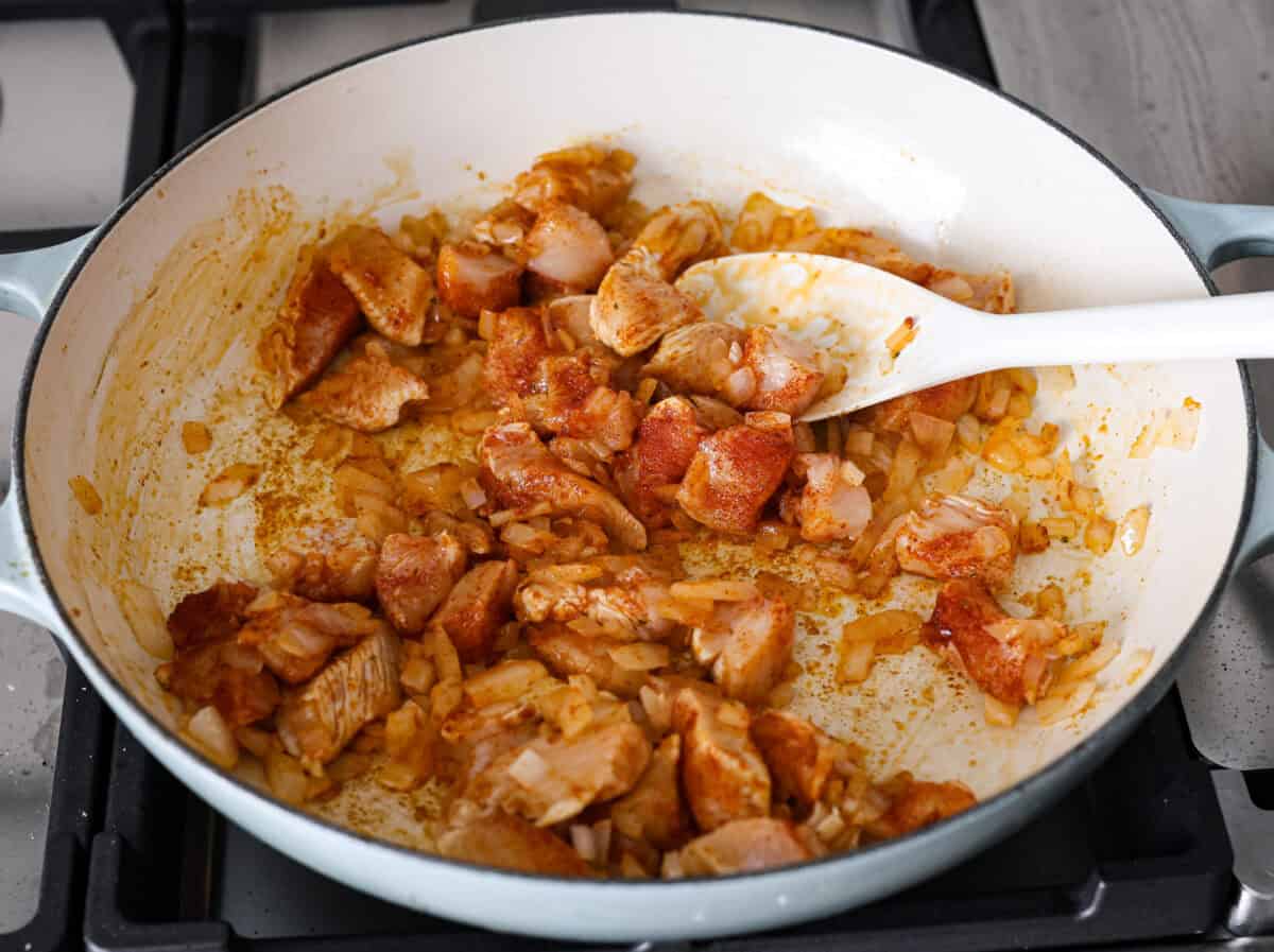 Angle shot of chicken, bullion, garlic powder, and paprika in the skillet with the onions. 