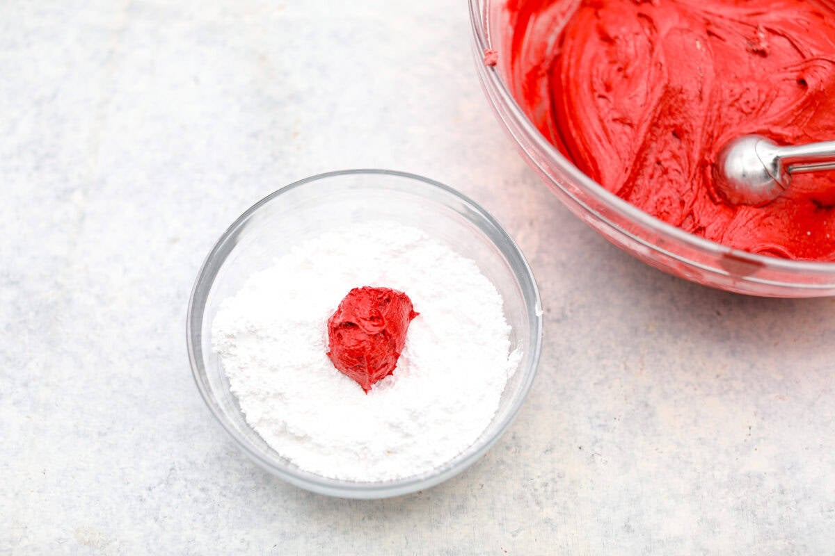 Overhead shot of a scoop of dough in a bowl of powdered sugar. 