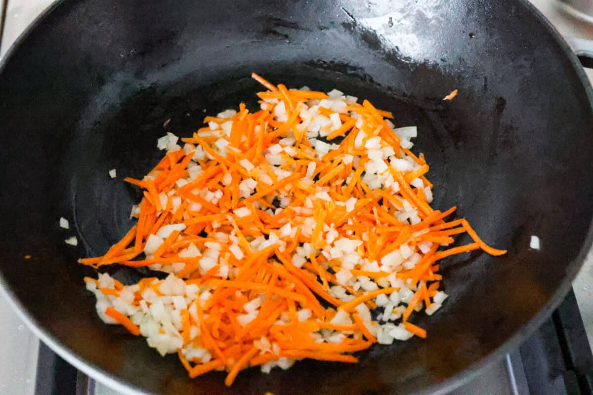 Overhead shot of carrots, onions and sesame oil cooking in a skillet. 