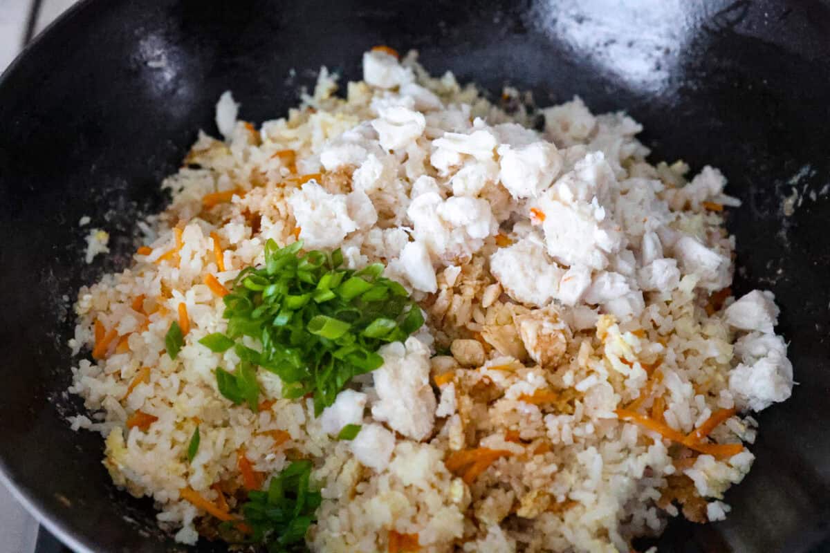 Angle shot of the crab,  green onions, soy sauce and lime juice on top of the rice, veggie and egg mixture. 