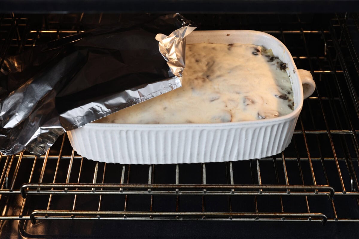 Side shot of mushroom lasagna cooking in the oven with someone taking the tin foil off. 