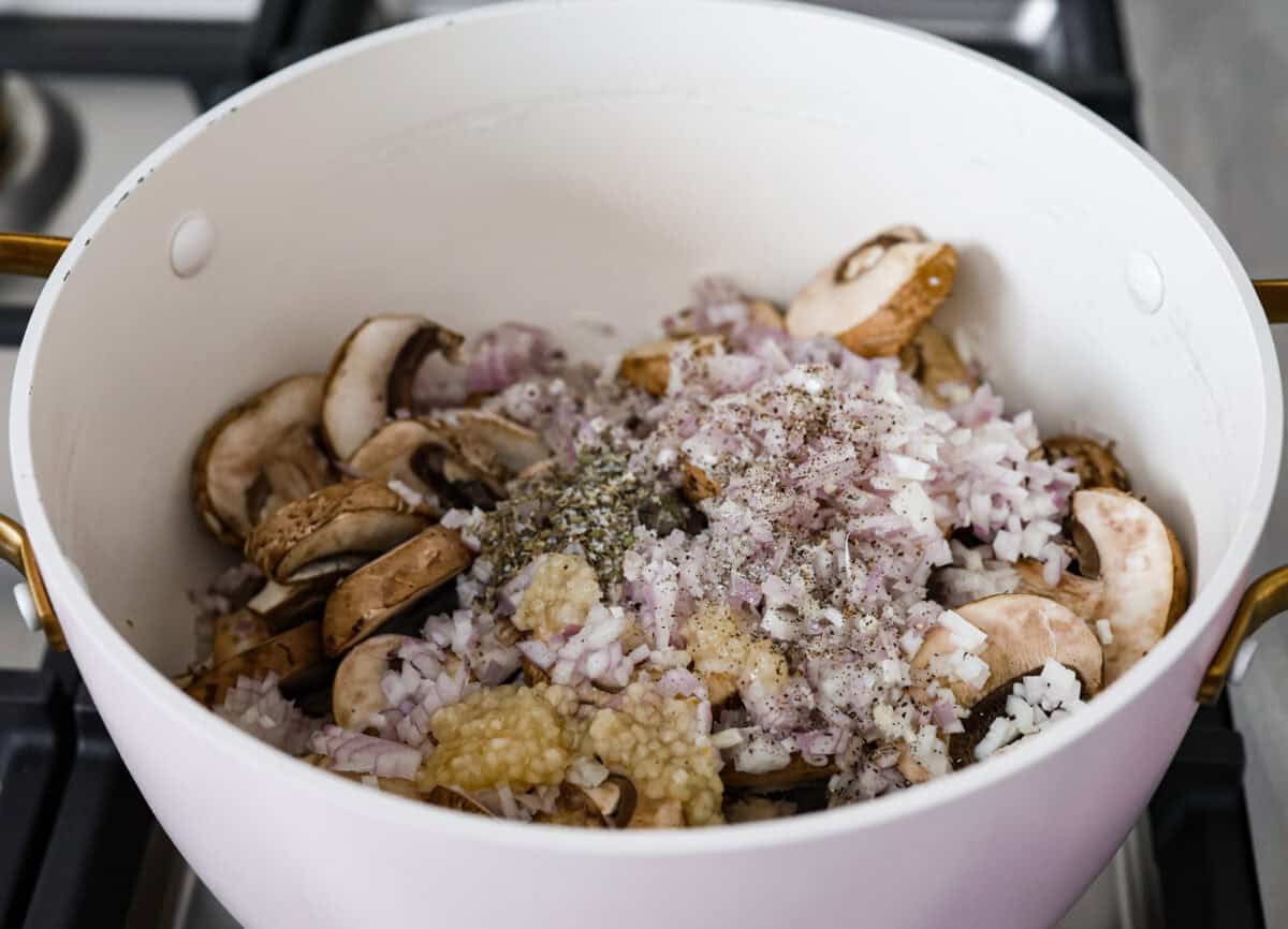 Angle shot of mushrooms, shallots, garlic and seasonings in a pot on the stove. 