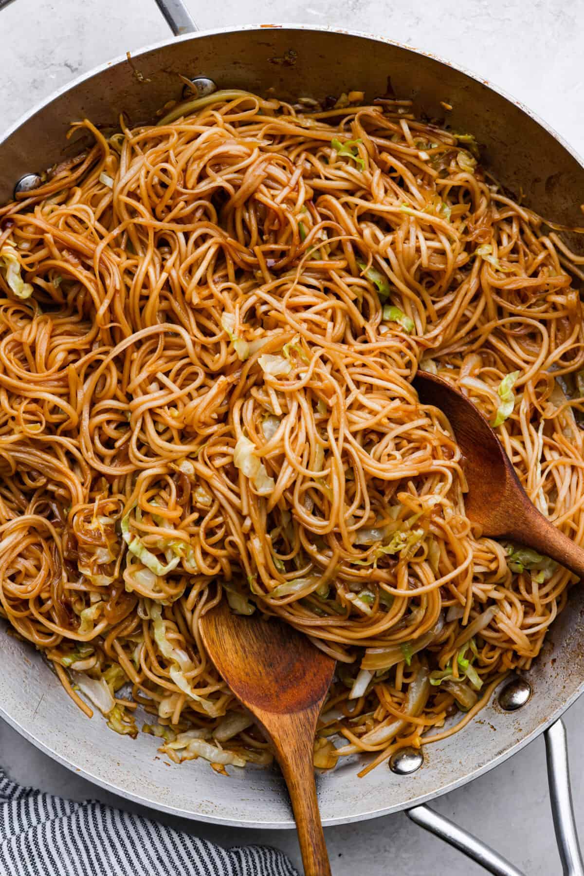 Overhead shot of Panda Express chow mein in a pan with two wooden serving spoons. 