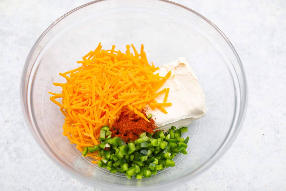 Overhead shot of cheddar cheese, cream cheese, jalapeño, and bbq rub seasoning in a bowl. 