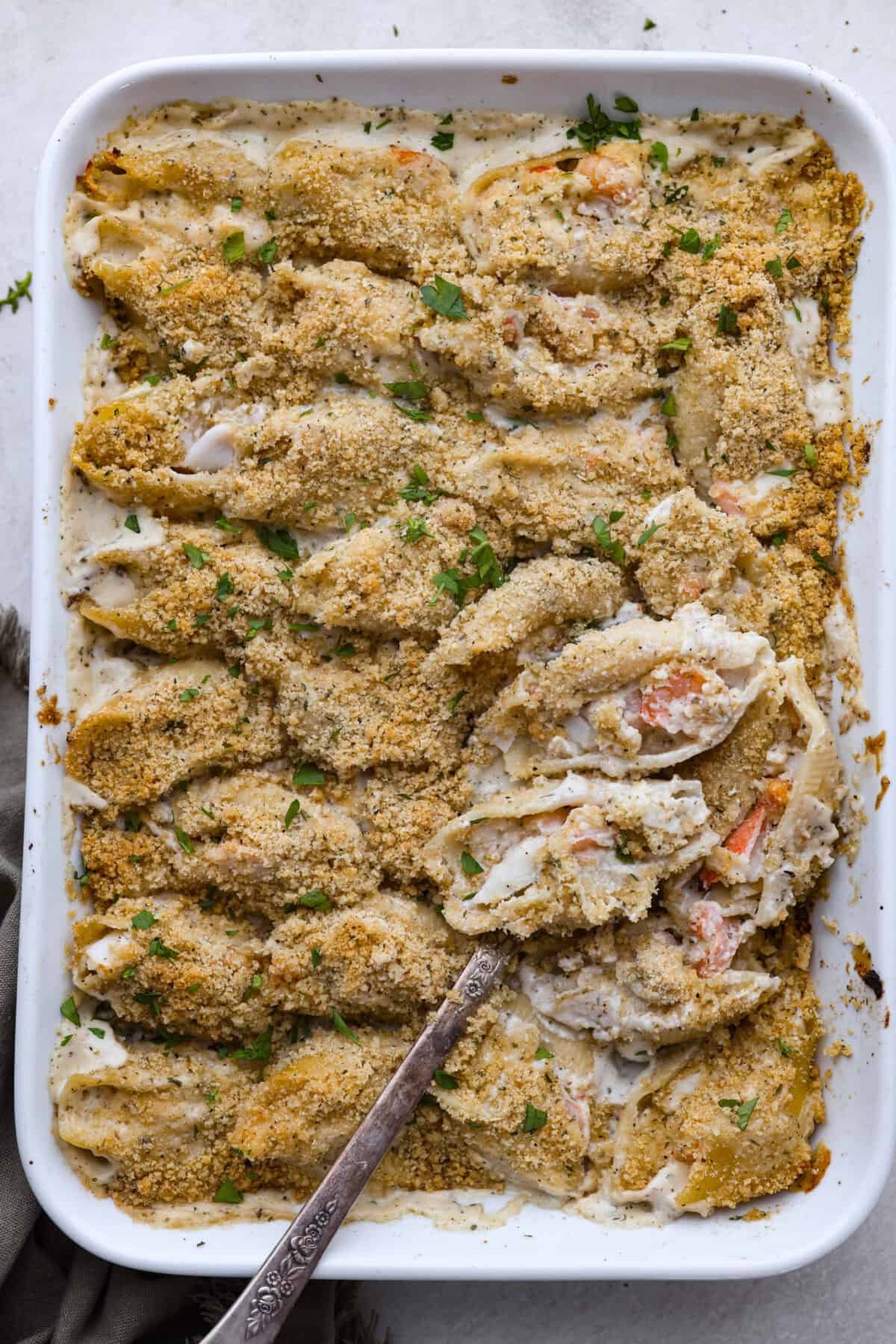 Overhead shot of a baking dish with seafood stuffed shells and a serving spoon. 