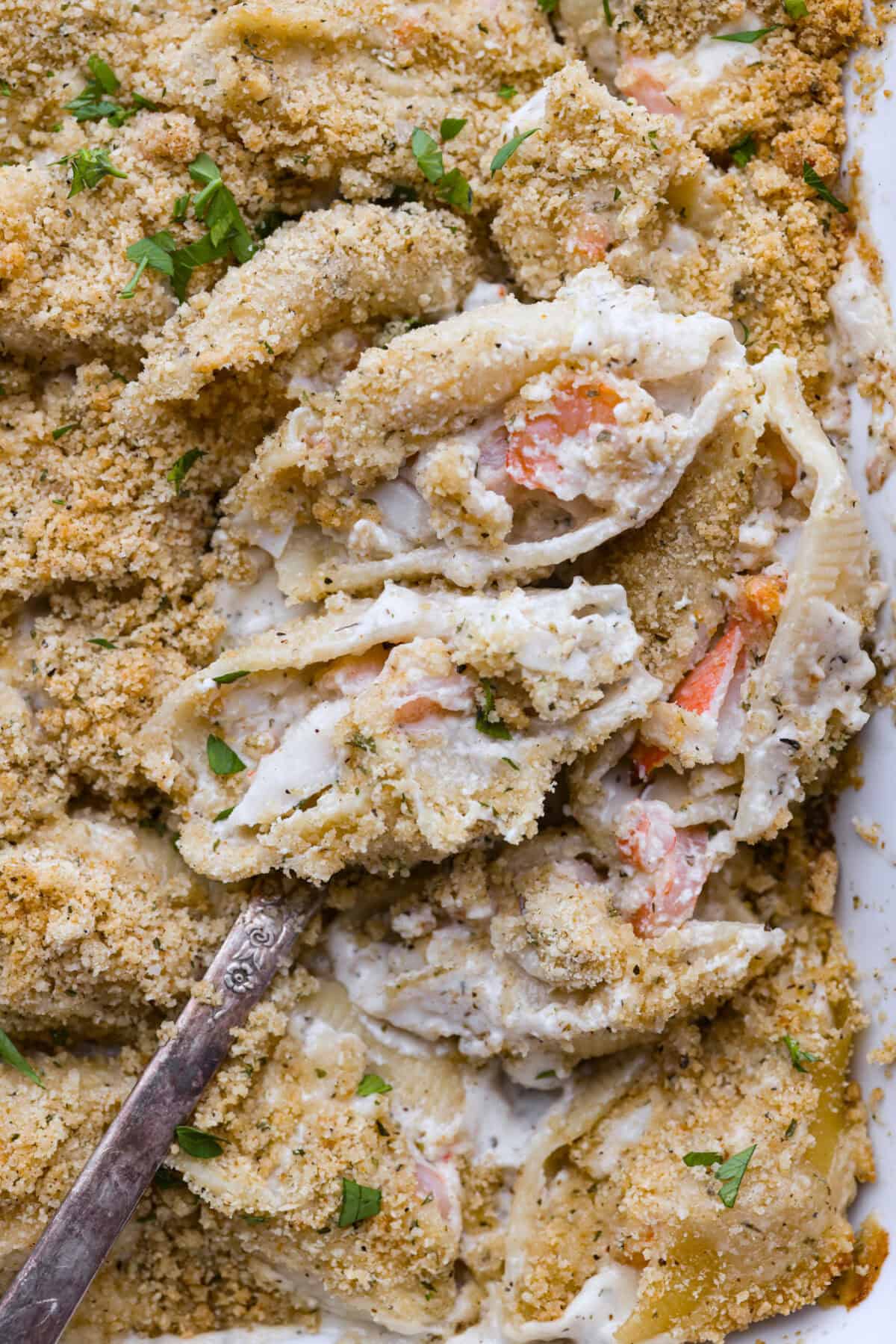 Close up shot of seafood stuffed shells on a serving spoon in the baking dish. 